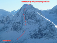 SV stena Taskedalsfjellet (1509 m, oblasť Innfjorden) s vyznačenou líniou (prvo?)zjazdu SV stenou (S3+/S4, E3, 40-50° na 600 m, červený ťažký, prevýšenie na dno doliny 930 m), fotené 9.2.2013 z Nonstinden, poznámka: v názvoch kopcov tejto oblasti je chaos a Taskedalsfjellet je niekedy označovaný ako Gronfonnfjellet